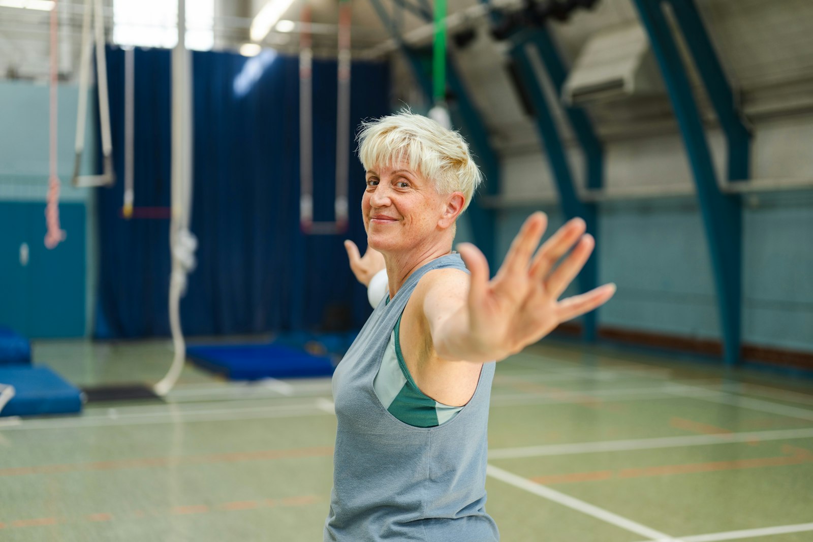 Smiling older woman stretching her arms out during an exercise class in a sports hall