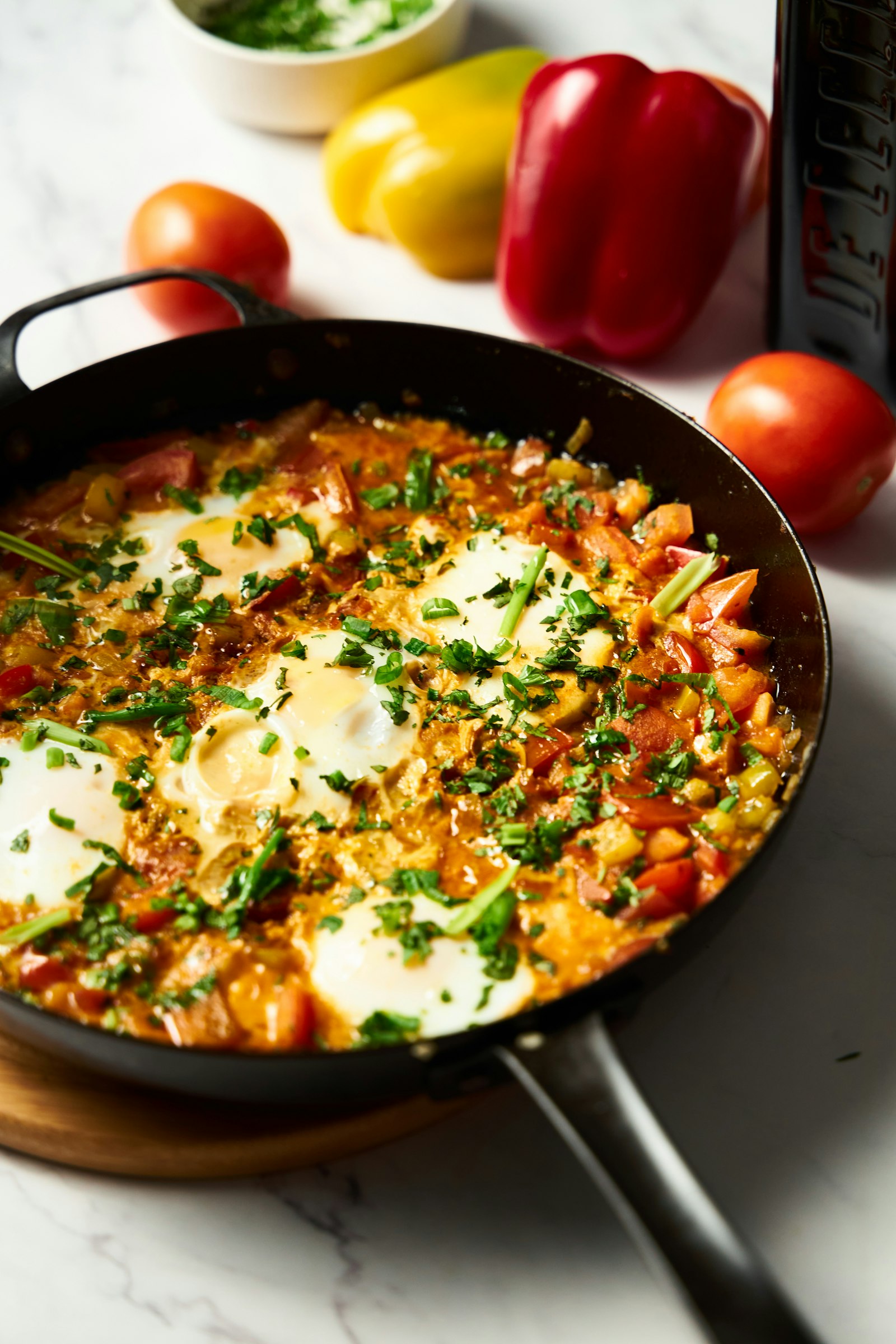 Shakshuka with eggs in a spiced tomato and pepper sauce, topped with chopped herbs, in a black skillet